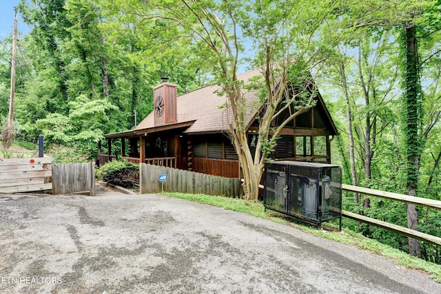 exterior space featuring fence, log siding, a shingled roof, a chimney, and covered porch