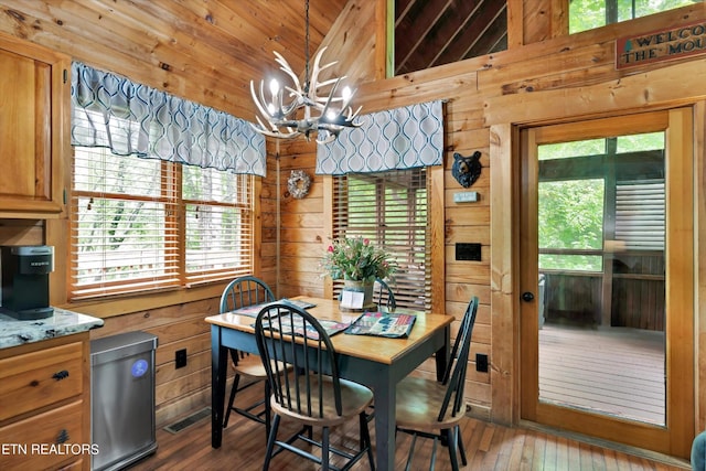 dining area with wooden walls, vaulted ceiling, hardwood / wood-style flooring, and a notable chandelier