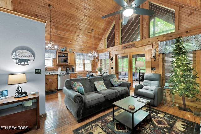living room featuring wood walls, light wood-style flooring, ceiling fan with notable chandelier, and high vaulted ceiling