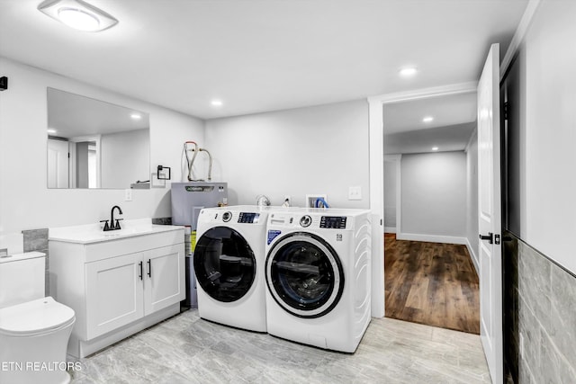 clothes washing area featuring recessed lighting, a sink, water heater, and washer and dryer