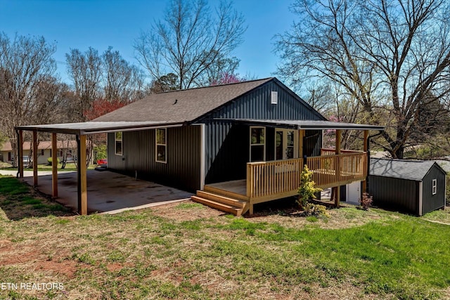 back of property featuring an outdoor structure, a deck, roof with shingles, a shed, and a lawn
