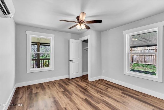 unfurnished bedroom with baseboards, a wall mounted AC, and wood finished floors