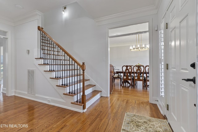entrance foyer with a notable chandelier, light wood finished floors, baseboards, visible vents, and stairway