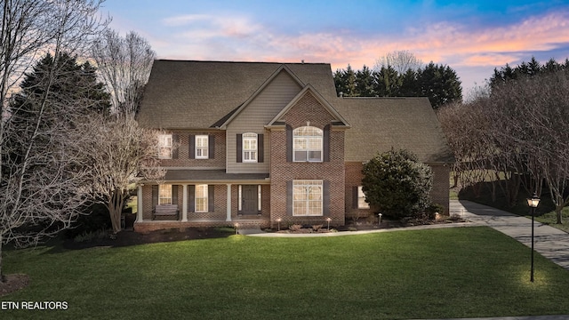 view of front facade with roof with shingles, covered porch, a front lawn, and brick siding