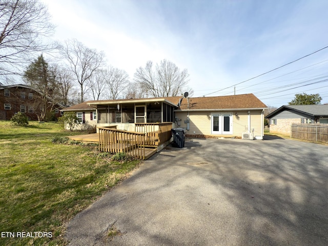 view of front of home featuring a front lawn, a wooden deck, fence, a sunroom, and driveway