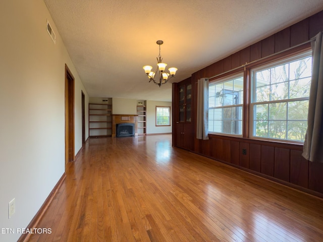 unfurnished dining area featuring visible vents, an inviting chandelier, a fireplace, light wood-style floors, and built in shelves