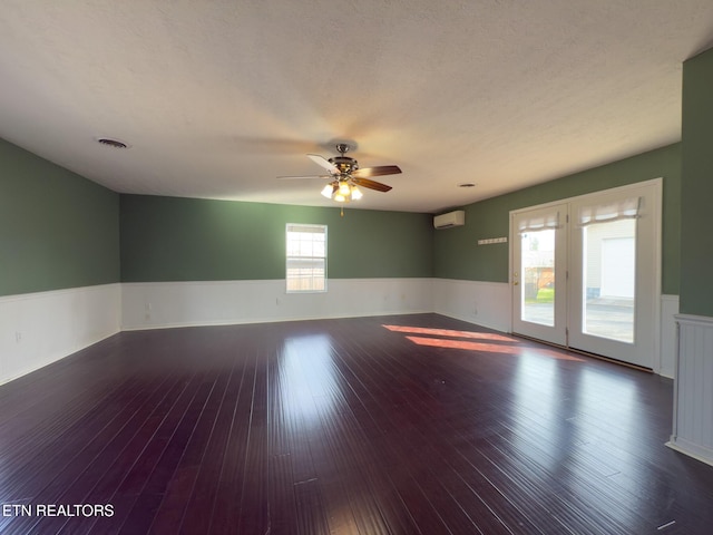 unfurnished room featuring wood-type flooring, visible vents, a wall unit AC, a wainscoted wall, and a ceiling fan