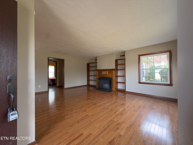 unfurnished living room with a fireplace with flush hearth, a textured ceiling, light wood-style flooring, and a wealth of natural light