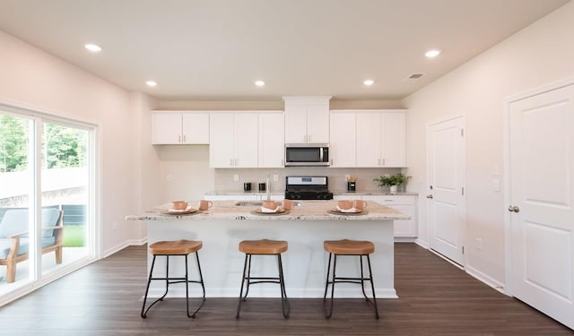 kitchen featuring a breakfast bar, white cabinetry, stainless steel microwave, a kitchen island, and gas range oven