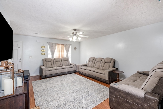 living room featuring baseboards, a textured ceiling, ceiling fan, and wood finished floors