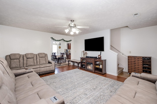 living area featuring stairway, a textured ceiling, a ceiling fan, and wood finished floors