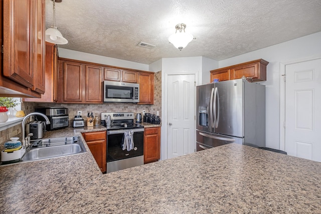 kitchen with brown cabinetry, decorative backsplash, visible vents, a sink, and appliances with stainless steel finishes