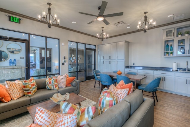 living room with visible vents, ornamental molding, light wood finished floors, and ceiling fan with notable chandelier