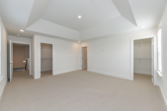 unfurnished bedroom with a spacious closet, light carpet, a raised ceiling, and a closet
