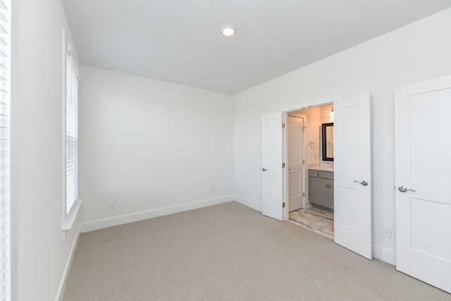 unfurnished bedroom with baseboards, light carpet, and ensuite bath