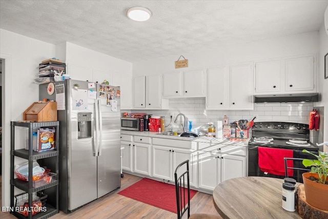 kitchen with light countertops, white cabinetry, under cabinet range hood, a sink, and stainless steel appliances