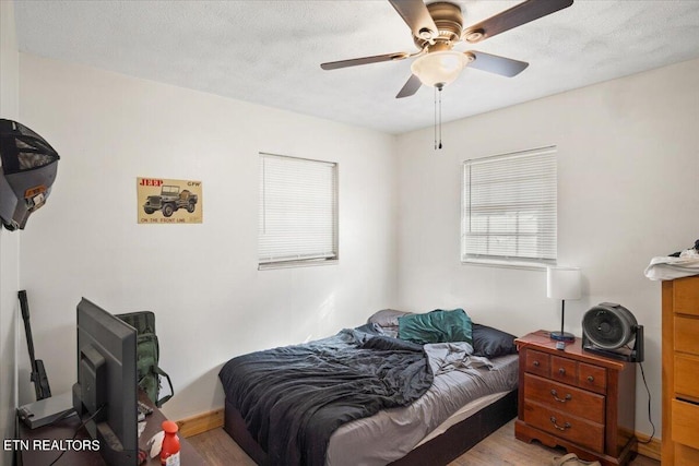bedroom featuring baseboards, a textured ceiling, ceiling fan, and wood finished floors