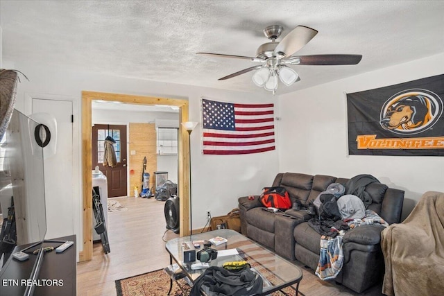 living room featuring a ceiling fan, light wood-style flooring, and a textured ceiling