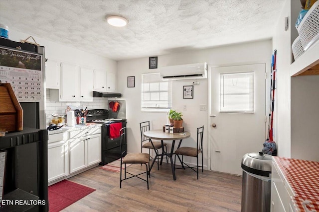 kitchen featuring decorative backsplash, black electric range oven, under cabinet range hood, a wall mounted AC, and white cabinets