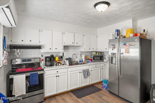 kitchen with wood finished floors, a sink, light countertops, under cabinet range hood, and stainless steel appliances