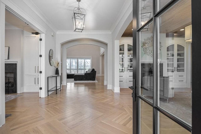 foyer entrance with arched walkways, ornamental molding, baseboards, and a notable chandelier
