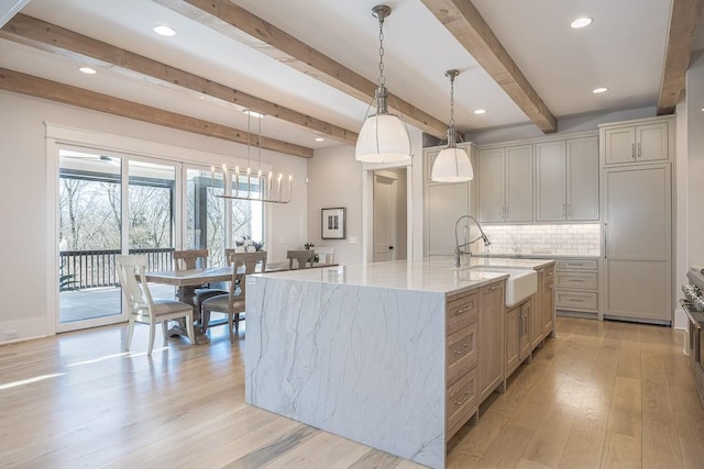 kitchen featuring light stone countertops, beamed ceiling, a sink, light wood finished floors, and backsplash