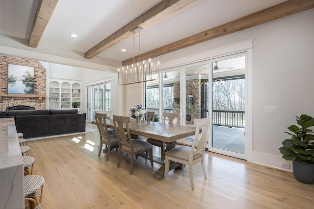 dining area with a brick fireplace, a notable chandelier, beam ceiling, and light wood finished floors
