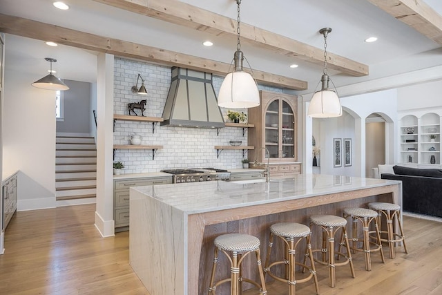 kitchen with premium range hood, decorative backsplash, open shelves, and a center island with sink