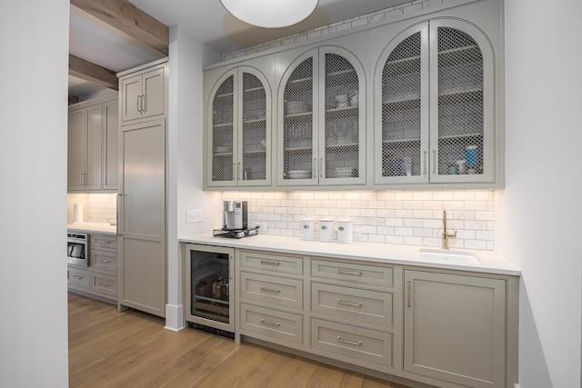 bar featuring wine cooler, oven, a sink, light wood-style flooring, and backsplash