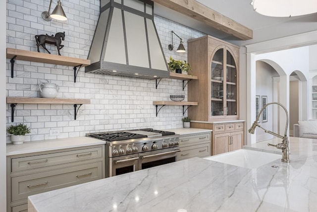 kitchen with wall chimney range hood, open shelves, a sink, decorative backsplash, and double oven range