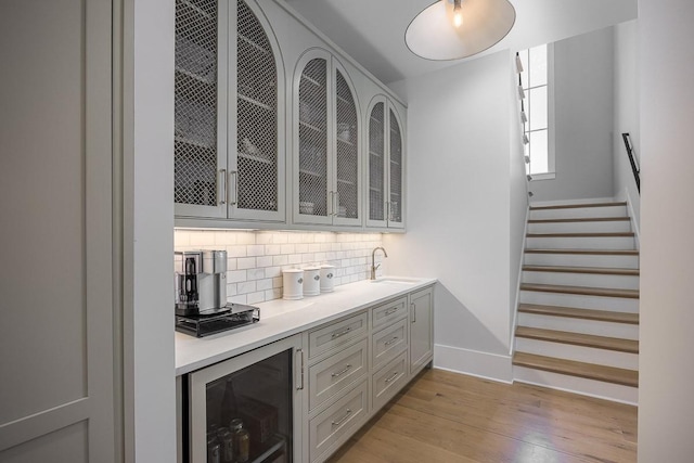 bar with wine cooler, light wood-style floors, baseboards, a sink, and backsplash