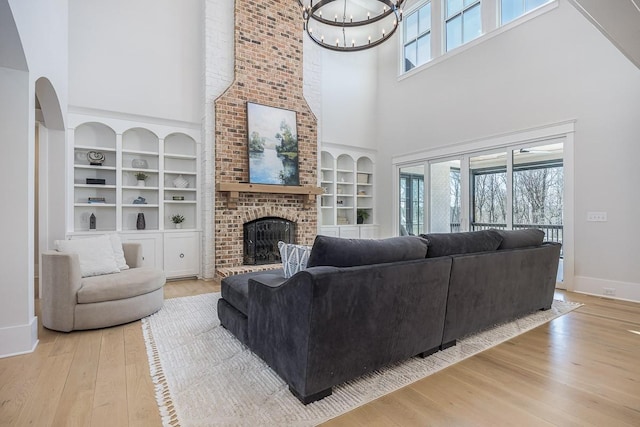 living room with a high ceiling, an inviting chandelier, a brick fireplace, built in shelves, and hardwood / wood-style floors