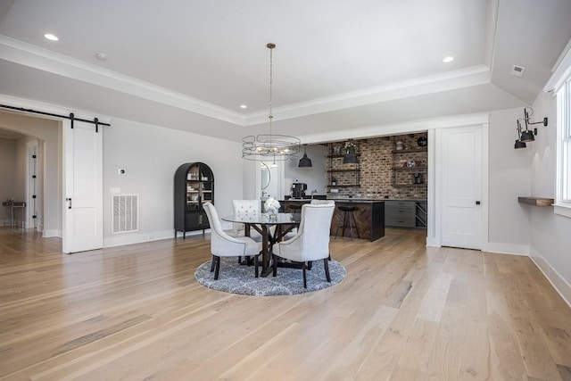 dining space with visible vents, arched walkways, a barn door, light wood finished floors, and a tray ceiling