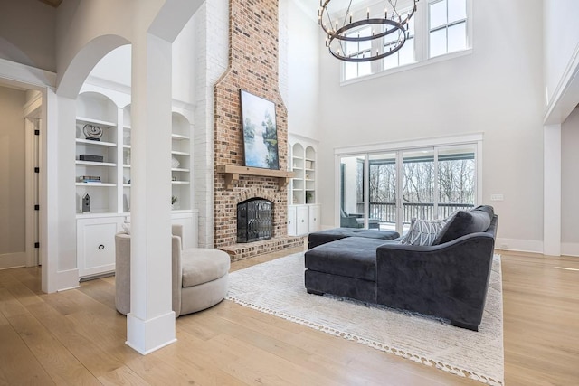living room with baseboards, a fireplace, light wood-type flooring, and a towering ceiling