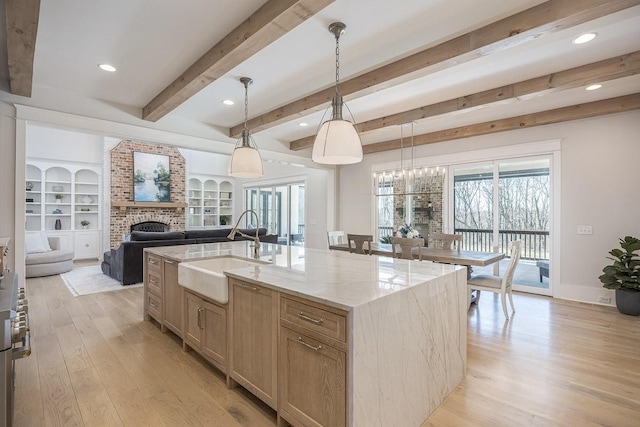 kitchen with light stone counters, a sink, light wood-style floors, a fireplace, and beamed ceiling