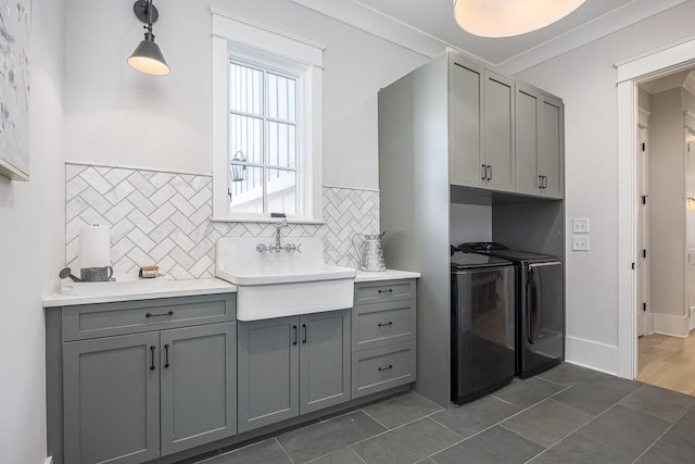 kitchen featuring a sink, decorative backsplash, gray cabinetry, and washing machine and clothes dryer