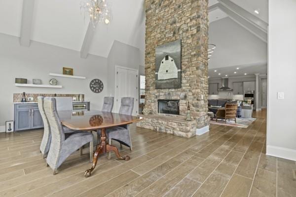 dining space featuring a fireplace, high vaulted ceiling, baseboards, beamed ceiling, and a chandelier