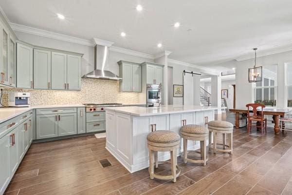 6209 Tall Timbers Rd, Franklin, TN 37067 - kitchen with a kitchen island with sink, a barn door, wall chimney range hood, appliances with stainless steel finishes, and tasteful backsplash