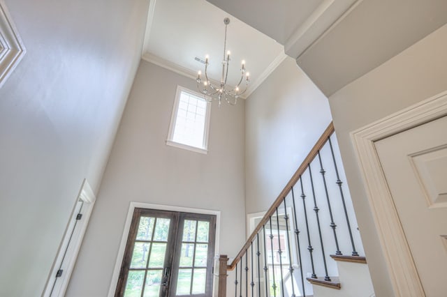 entrance foyer with french doors, ornamental molding, a notable chandelier, a high ceiling, and stairs