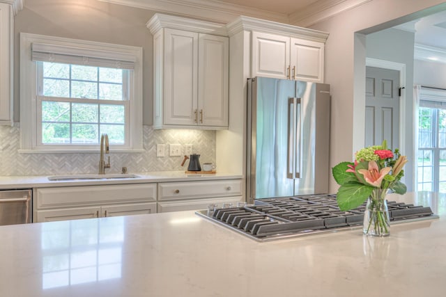 kitchen with crown molding, tasteful backsplash, a sink, white cabinets, and stainless steel appliances