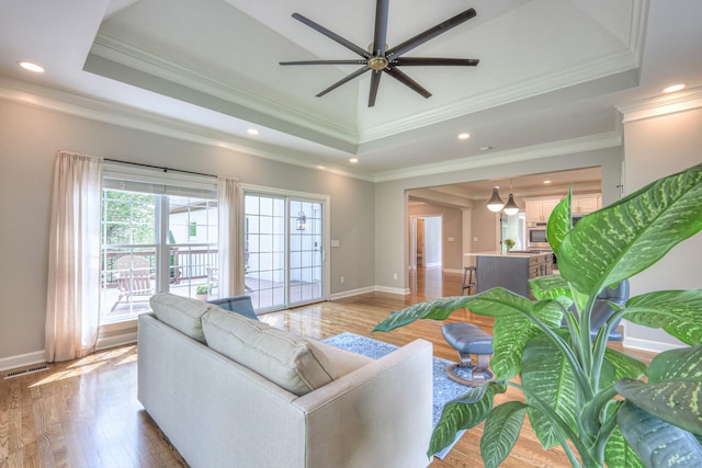 living room featuring visible vents, light wood-style flooring, a raised ceiling, and baseboards