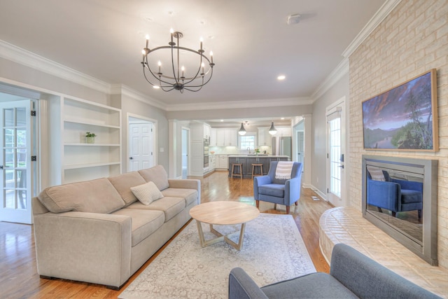 living room with a fireplace, light wood-style floors, a chandelier, built in shelves, and ornamental molding