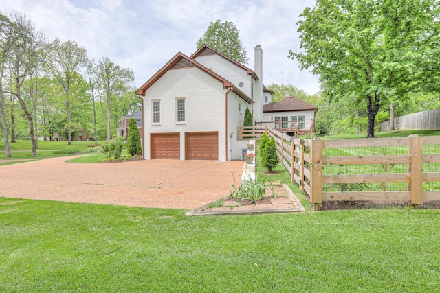 view of property exterior featuring fence, driveway, a chimney, an attached garage, and a yard