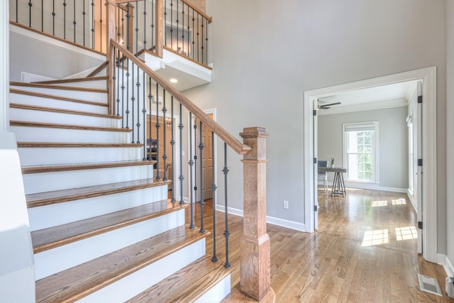 stairs with crown molding, visible vents, a towering ceiling, wood finished floors, and baseboards