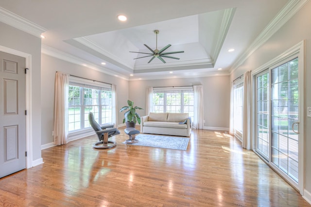 living area featuring ceiling fan, plenty of natural light, a tray ceiling, and light wood-type flooring