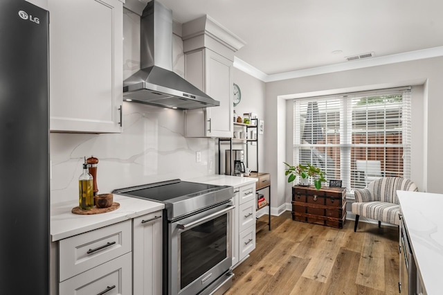 8542 Sawyer Brown Rd, Nashville, TN 37221 - kitchen with crown molding, stainless steel range with electric stovetop, wall chimney exhaust hood, freestanding refrigerator, and visible vents