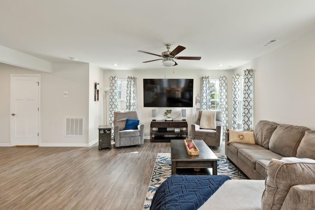 living area with wood finished floors, a wealth of natural light, ceiling fan, and visible vents
