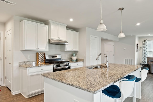 kitchen with visible vents, wood finished floors, stainless steel gas range oven, under cabinet range hood, and a sink