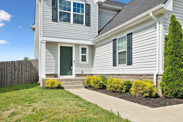 entrance to property featuring fence, a shingled roof, and a lawn