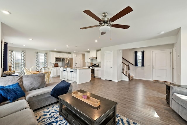 living area with wood finished floors, baseboards, ceiling fan, stairway, and recessed lighting